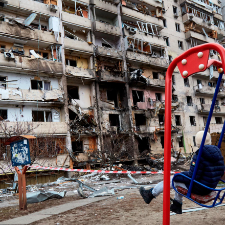 Ein Kind schaukelt vor einem Wohnhaus, das durch einen Raketenangriff in Kiew beschädigt wurde