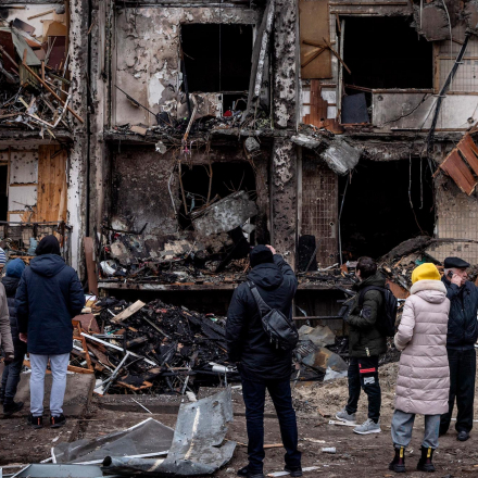 Menschen betrachten das Äußere eines beschädigten Wohnblocks, der von einem Raketenangriff in Kiew, Ukraine, getroffen wurde