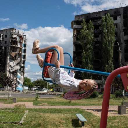 A child swings on a swing against the background of destroyed houses