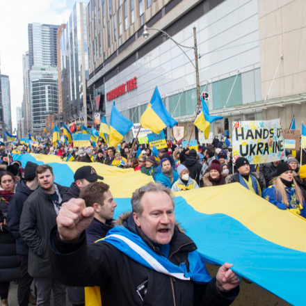 A large Ukrainian flag is carried through the streets of Toronto