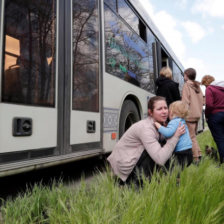 A woman holds a child next to a bus as civilians from Mariupol, including evacuees from Azovstal steel plant, travel in a convoy to Zaporizhzhia
