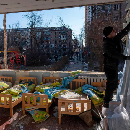 Ein Mann entfernt einen zerstörten Vorhang in einer durch Bomben zerstörten Schule, neben anderen Wohngebäuden in Kiew