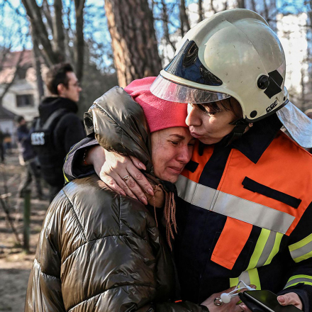 An evacuated resident is comforted by Svitlana Vodolaga, spokesperson for State Emergency Services of Ukraine outside a burning apartment building in Kyiv