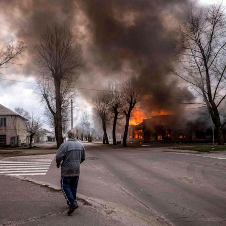 Ein Mann geht auf einem Bürgersteig, während ein Haus nach einem Beschuss in Severodonetsk, Region Donbass, brennt