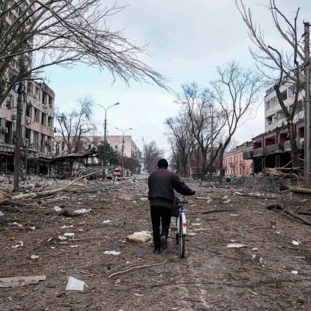 A man walks a bicycle down a street damaged by shelling in Mariupol