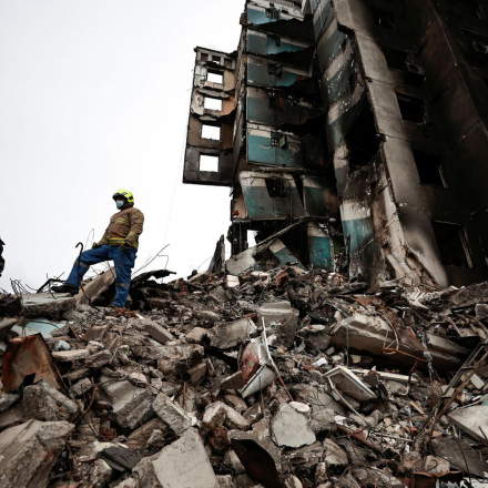 A rescuer stands on the rubble of a building destroyed by Russian shelling