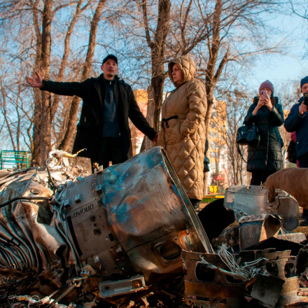 People stand next to fragments of military equipment on the street in the aftermath of an apparent Russian strike in Kharkiv